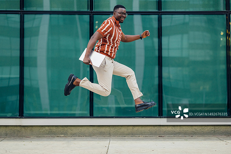 带着笔记本电脑跳跃的快乐年轻男商人图片素材