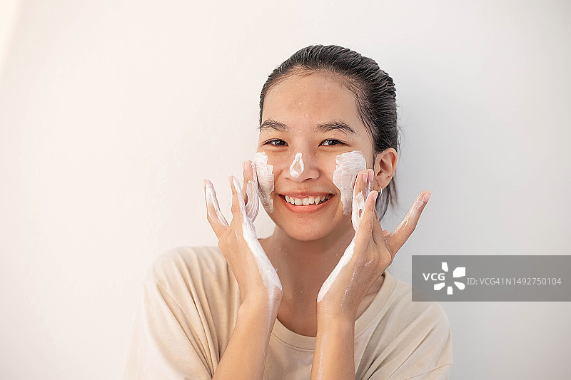 面部皮肤护理：有趣的亚洲女人用泡沫洁面皂清洁面部皮肤图片素材