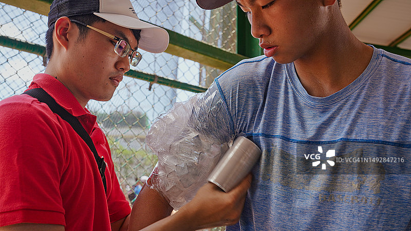 棒球比赛后，运动教练在休息区用冰袋为棒球运动员缓解手臂疼痛图片素材