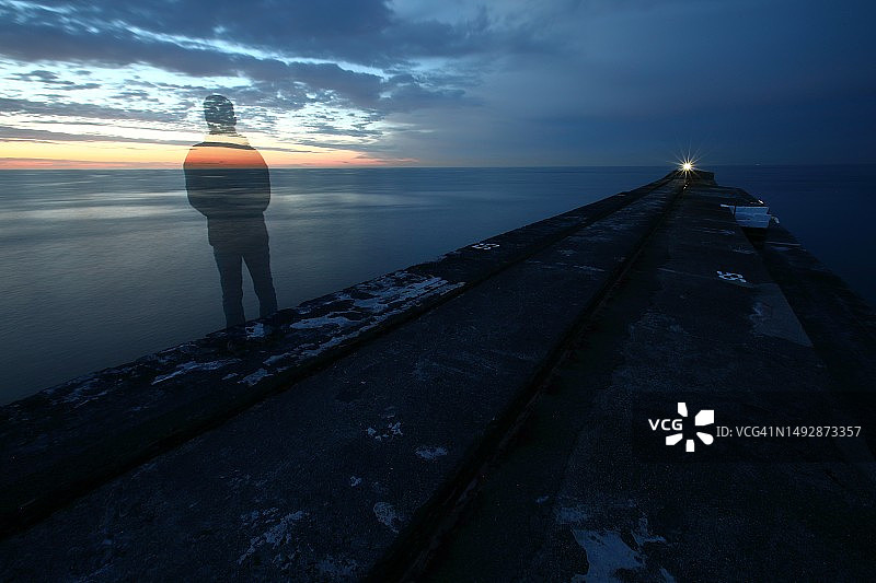 黄昏时分，独自站在防波堤上看海的人的剪影图片素材