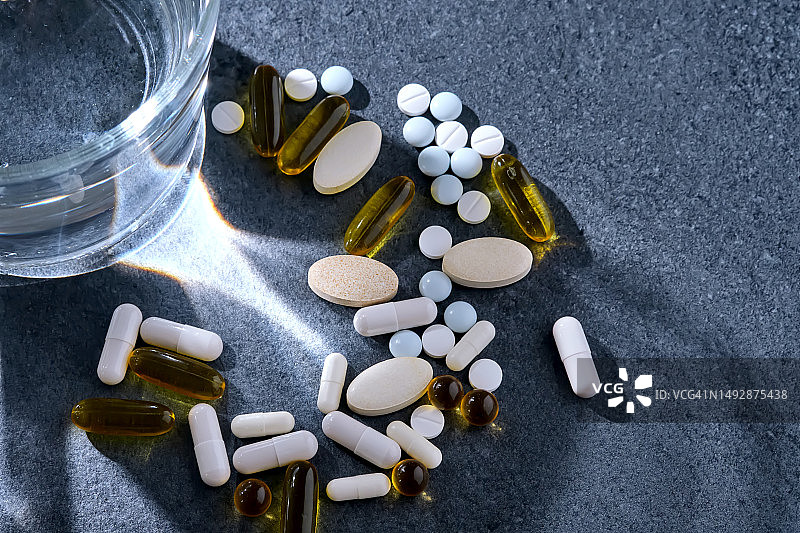 深色桌子上玻璃杯旁边的药片、维生素和膳食补充剂图片素材