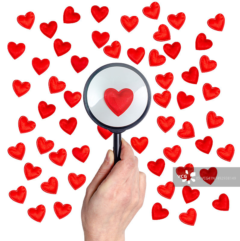 女性手指拿着放大镜，在红色爱心装饰上图片素材