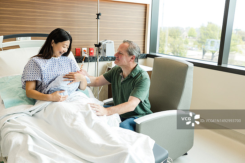 快乐的母亲看着宝宝，骄傲的父亲在一旁观看图片素材