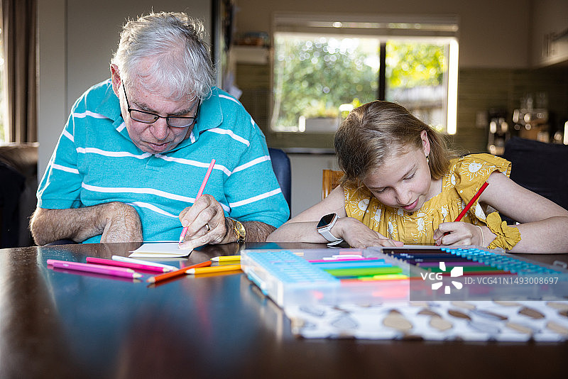 患有痴呆症的老年男人与小女孩在桌旁用彩色铅笔绘画图片素材