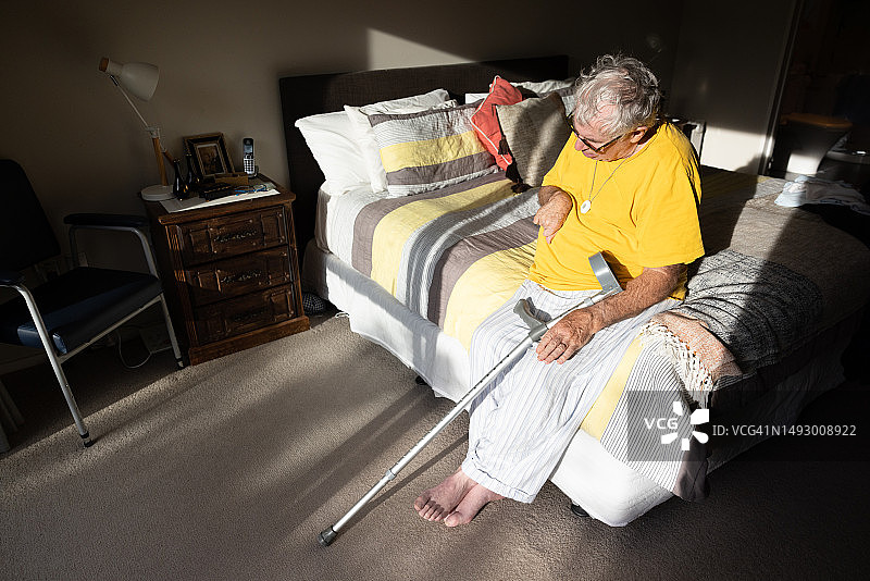 患有痴呆症的年长男人穿着睡衣，拄着拐杖坐在床边图片素材