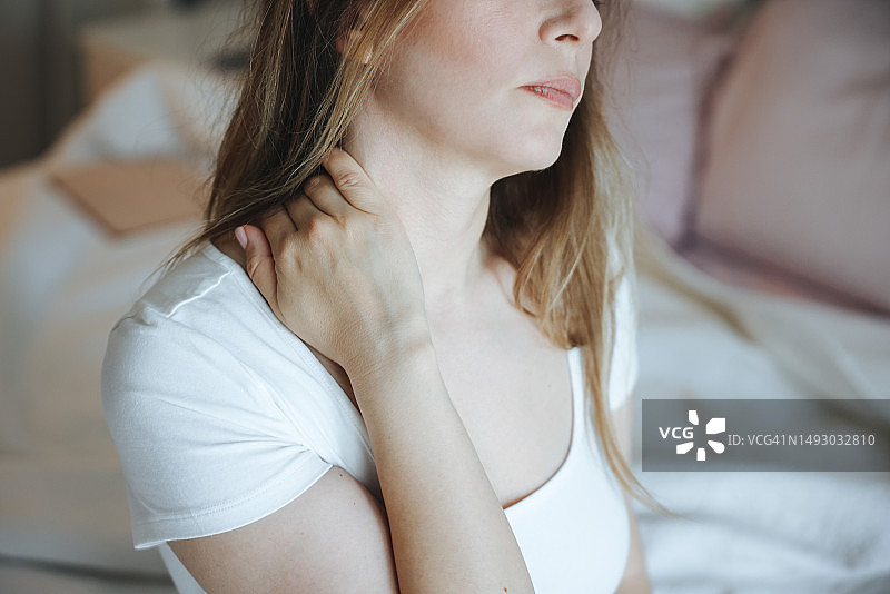 年轻女人在卧室里捂着脖子，感到疼痛图片素材