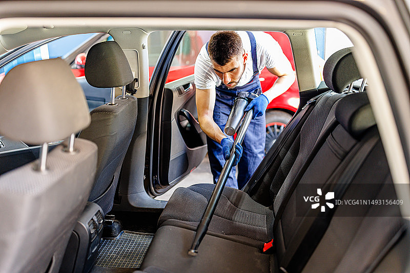 一个年轻男人用真空吸尘器清洁汽车内部图片素材