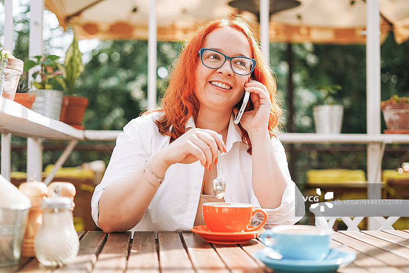 在咖啡馆露台上用手机喝咖啡的年轻红发女人图片素材