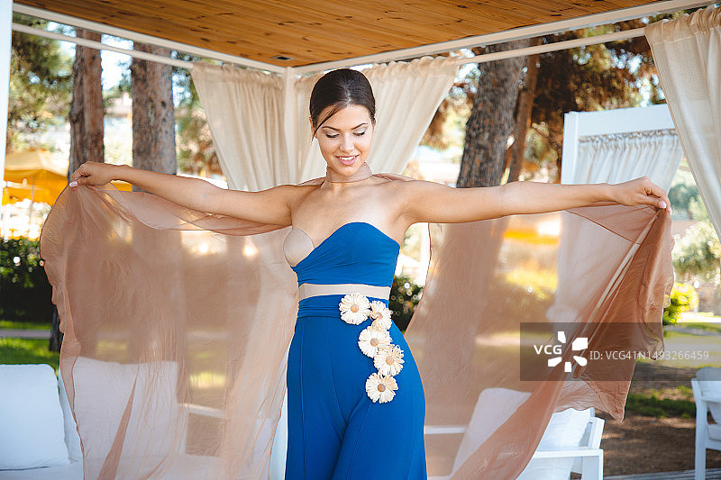 身穿蓝色无肩带长裙的年轻时尚女模特站在凉亭里，撩起面纱图片素材