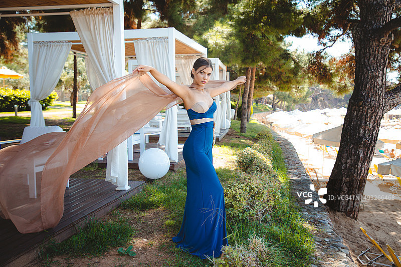 穿着蓝色无肩带长裙，站在公园凉亭里，撩起面纱的年轻时尚模特图片素材