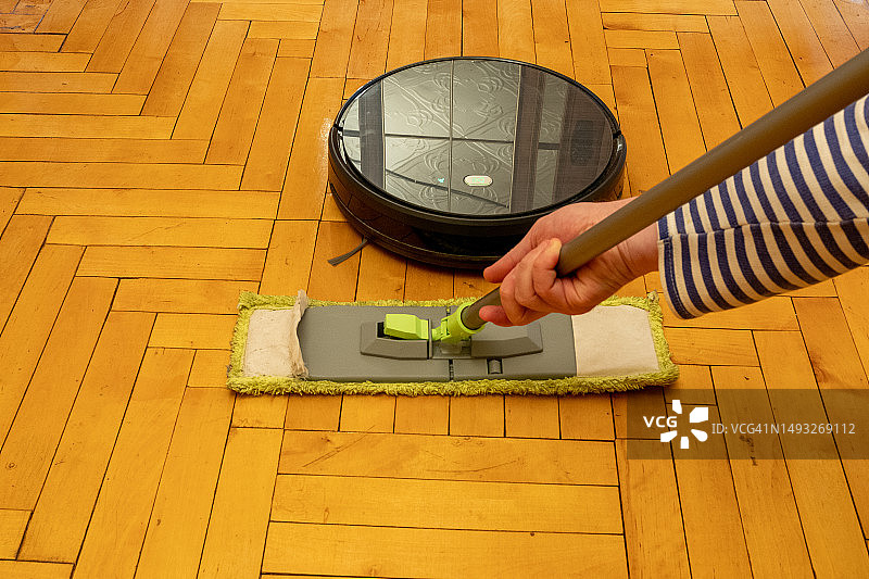 在光亮漆木地板上，扫地机器人与传统拖把的对比图片素材