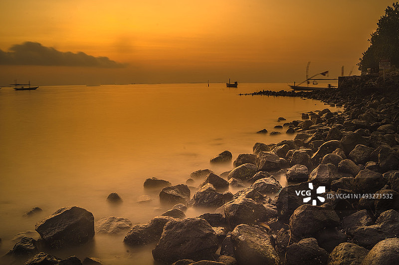 美丽的日出云彩，前景是岩石和肯杰兰水面上的动态船只，印度尼西亚泗水图片素材