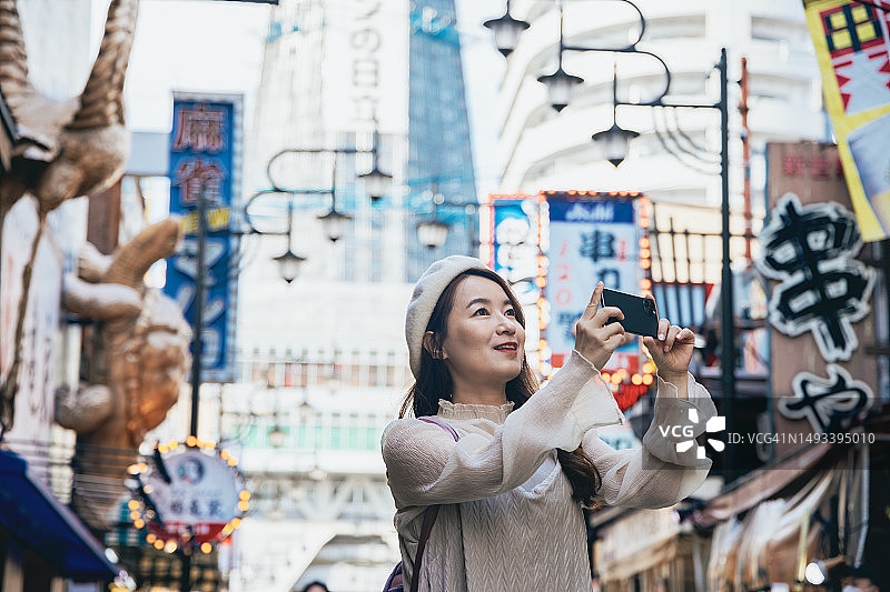 亚洲女性在日本大阪通天阁观光，用智能手机拍摄通天阁和周围的景色图片素材