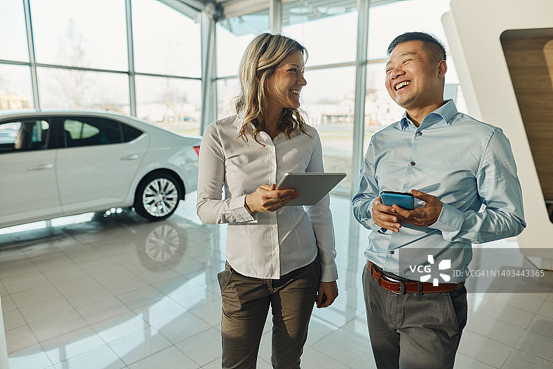 快乐的商务同事在汽车展厅使用无线技术时交谈图片素材