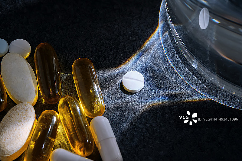 深色桌子上玻璃杯旁边的药片、维生素和膳食补充剂图片素材