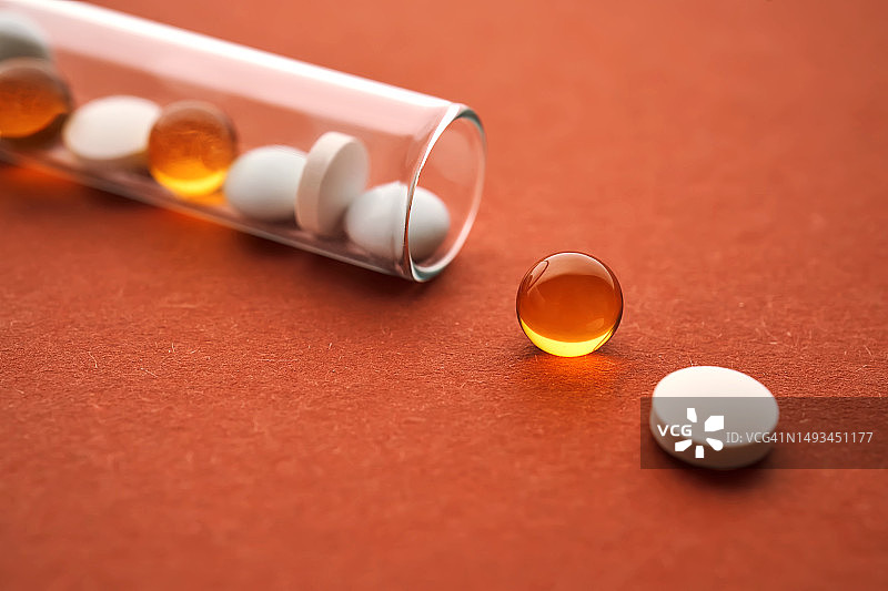 橙色背景试管中的药片、维生素和膳食补充剂图片素材