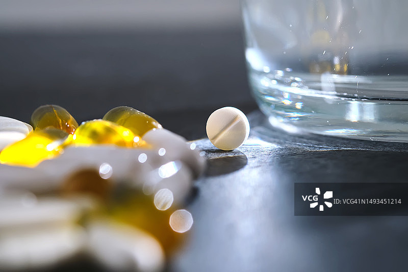 深色桌子上玻璃杯旁边的药片、维生素和膳食补充剂图片素材