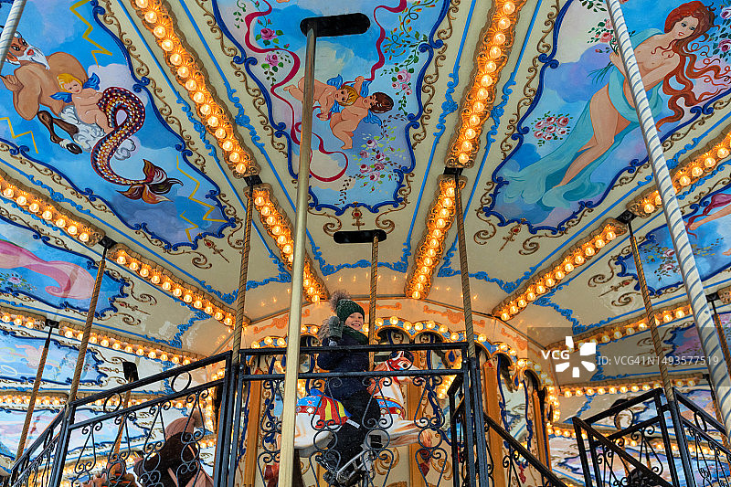 女孩在冬季集市的旋转木马上玩耍。新年假期儿童的欢乐旋转木马图片素材