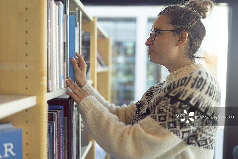 在图书馆里微笑女人从书架上取书的侧面照，冰岛图片素材