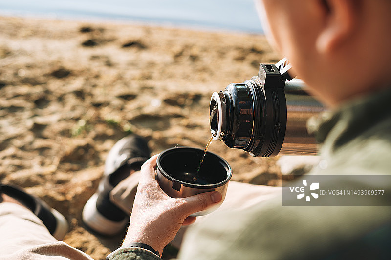 年轻男子在湖边徒步旅行，用保温瓶倒茶特写图片素材