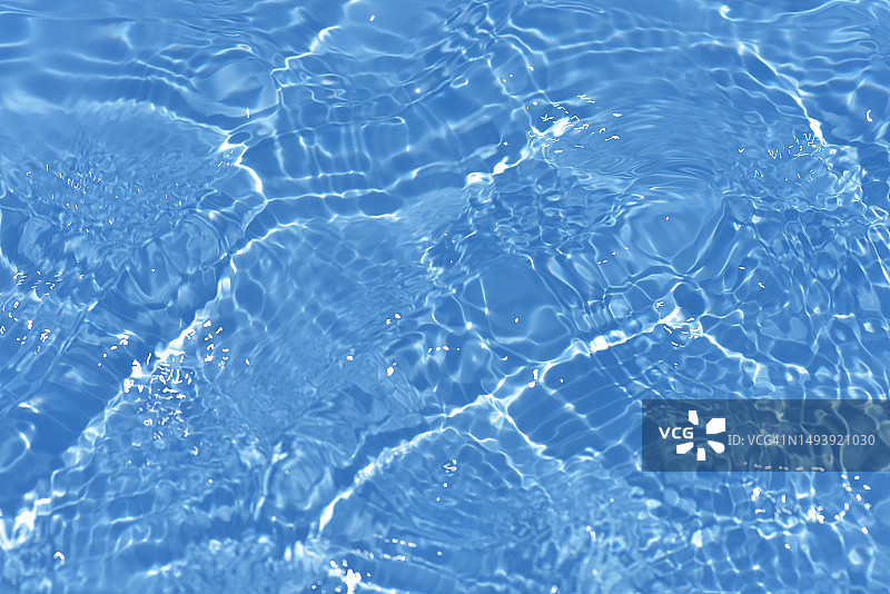 蓝蓝的水面上泛起涟漪。散焦模糊透明蓝色透明平静水面纹理与飞溅和气泡。水波与闪亮的图案纹理背景。图片素材