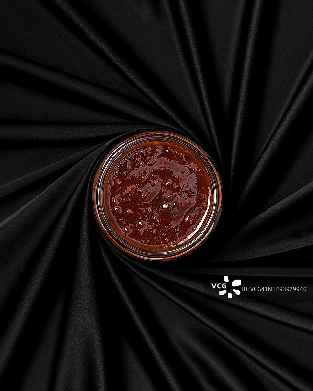 黑色粗麻布上的圆形红色辣酱罐，无盖，俯视，黑色背景，留白图片素材