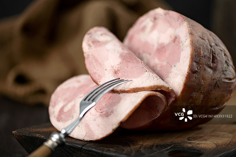 木板上切片的火腿，香肠末端，叉子上的火腿切片，深色背景，侧视图，特写图片素材