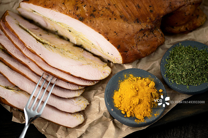 熏火鸡肉片，木板上用包装纸包裹并撒有香料，叉子上叉着肉块，俯视角度特写图片素材