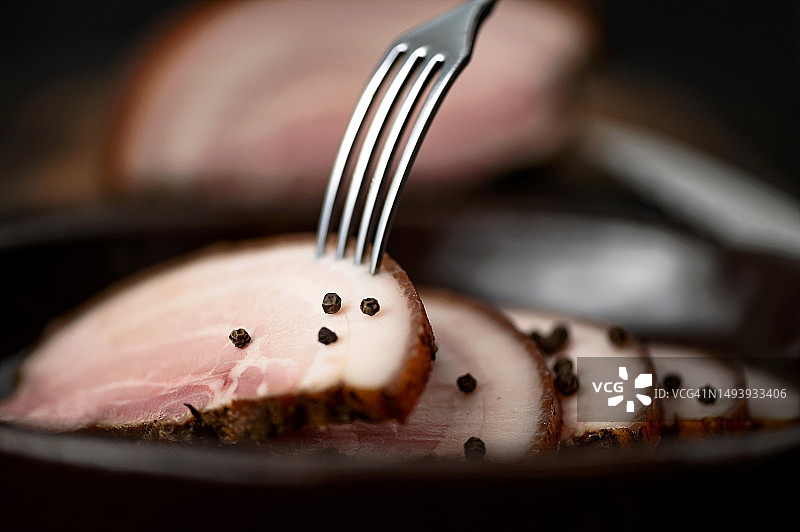 烟熏五花肉。盘中叉子上的牛腩片饰有黑胡椒。肉类烟熏肉。带肉的萨洛。特写。侧视图。柔焦。图片素材