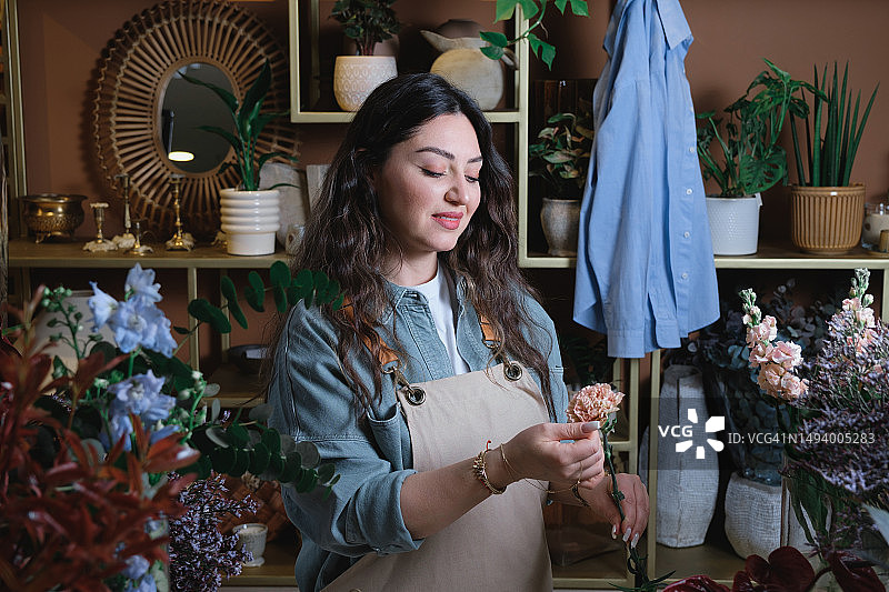 年轻女花艺师在温馨花店打理鲜花，制作精美现代花束。花艺，小本生意，零售概念，花店店员创作创意花束。图片素材