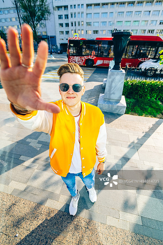 在城市街道上对着镜头微笑，手掌朝前的快乐年轻男人图片素材