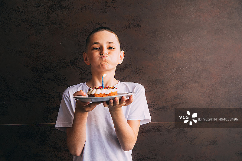 穿着白色T恤的苗条男孩手拿点燃蜡烛的蛋糕，准备吹灭图片素材