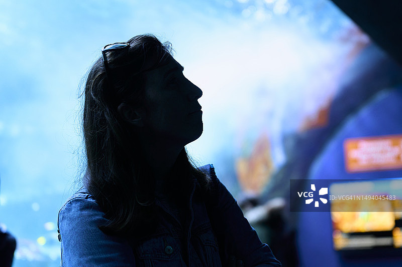 在水族馆看鱼的戴眼镜女人的深色轮廓图片素材