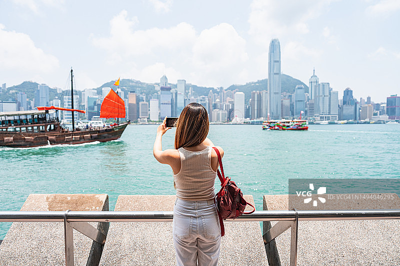 一位年轻的亚洲女游客用她的智能手机拍摄香港当地城市街道的美丽景色图片素材