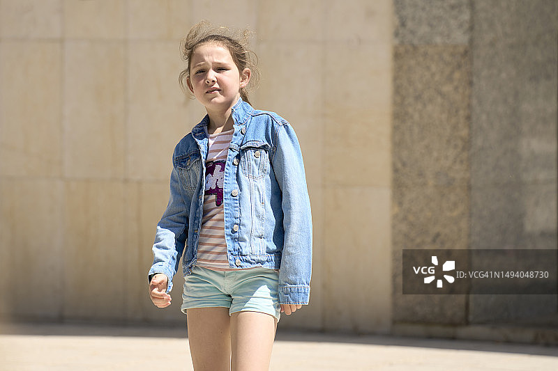 穿着休闲外套的可爱女孩站在街上，面向相机的正面肖像图片素材