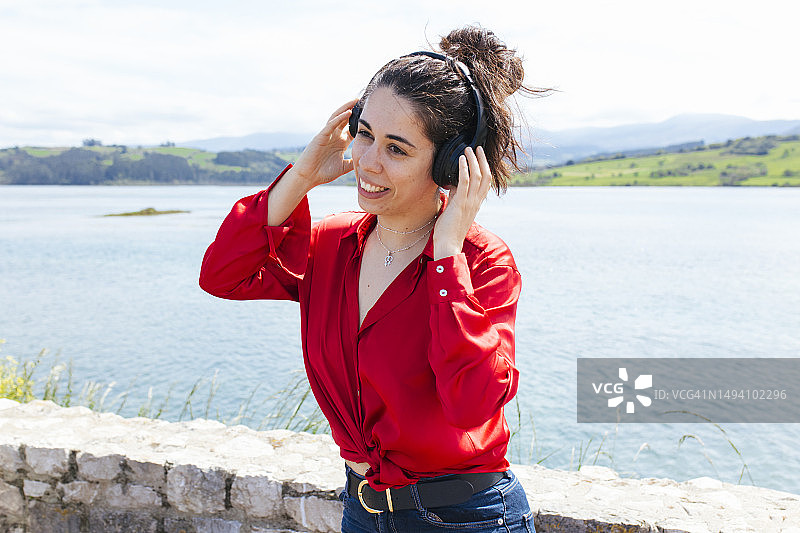 千禧一代女性在湖边戴着耳机听音乐图片素材