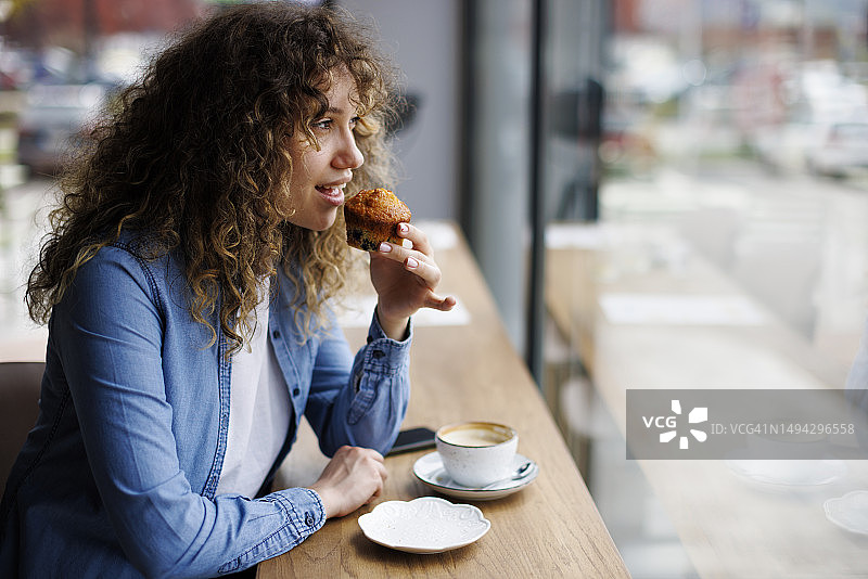 年轻女子在咖啡馆吃松饼喝咖啡图片素材