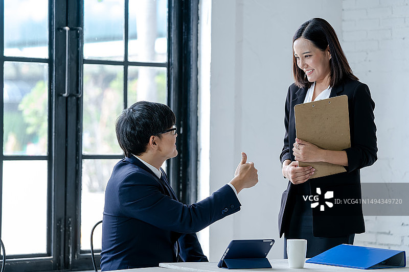 商务男士竖起大拇指，为办公室里的同事们微笑，金融概念图片素材