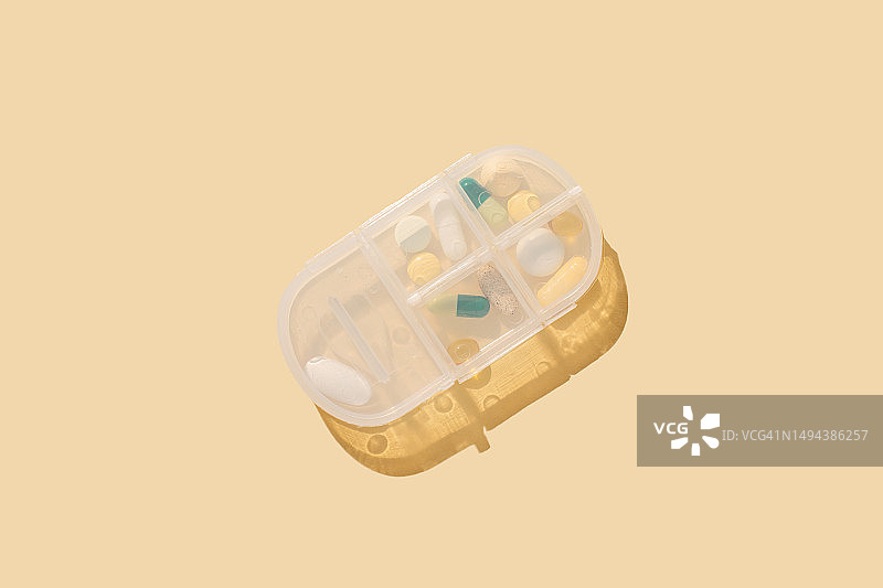 药丸整理盒特写。黄色背景上的药丸和胶囊盒。图片素材