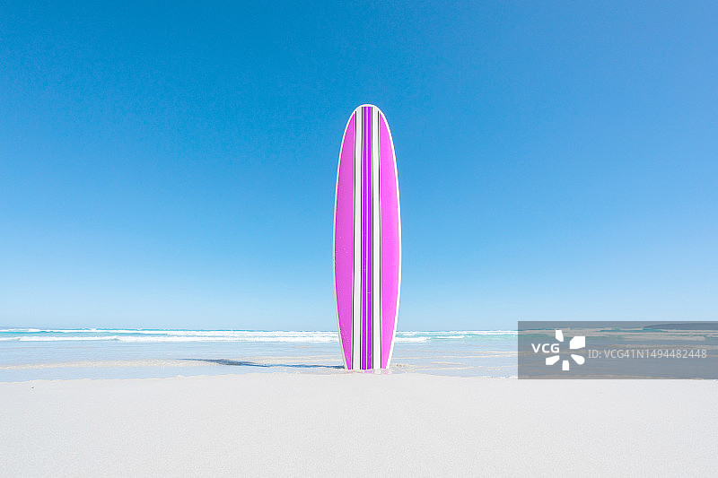 空旷沙滩上的粉紫色复古冲浪板，背景是海浪，蓝色天空留有文案空间图片素材