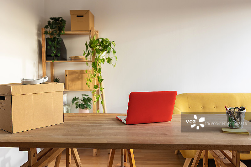 明亮的空旷工作场所房间，配有大型木桌、笔记本电脑、黄色沙发和办公用品图片素材