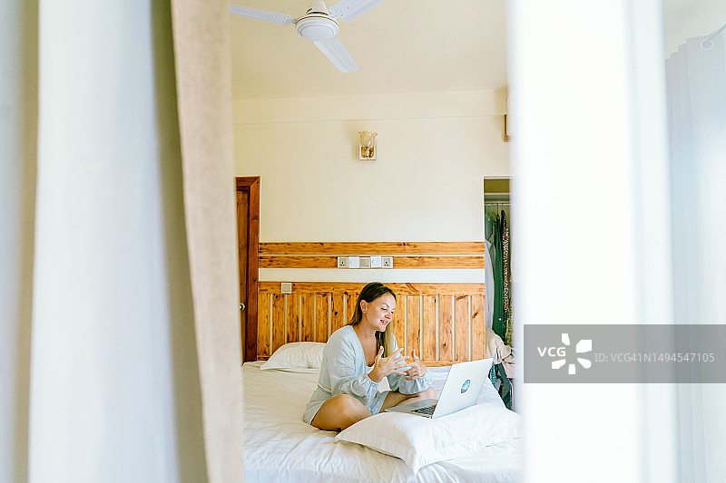 酒店房间床上穿蓝色睡衣女人用笔记本电脑图片素材