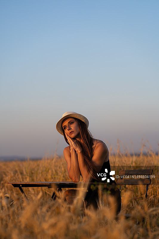 以色列麦田里，一位美丽而忧伤的年轻女人独自坐在桌旁的椅子上图片素材