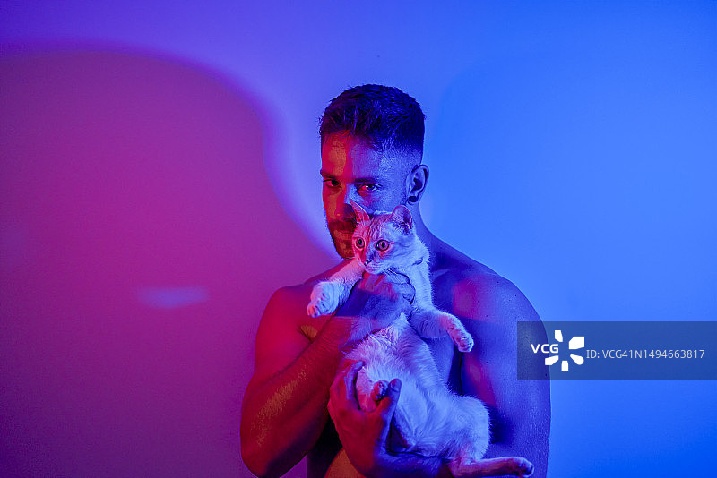 男人怀抱猫咪，沐浴在红蓝霓虹灯光中图片素材