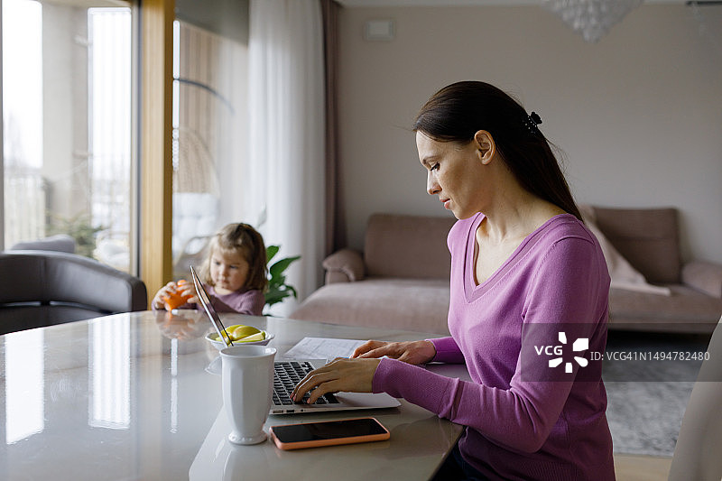 在家用笔记本电脑工作的女人和女儿图片素材