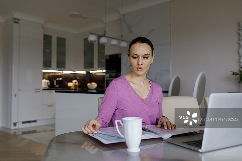 女人在餐桌旁使用笔记本电脑处理文件图片素材