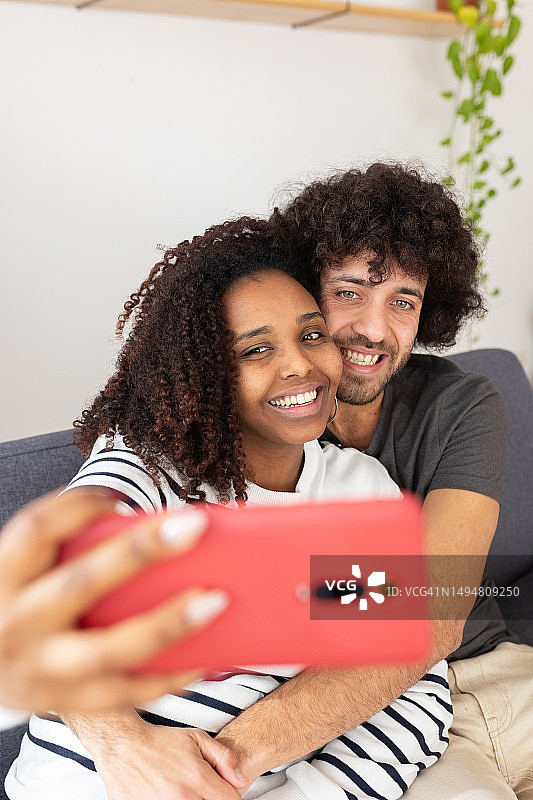 年轻的多种族夫妇在家用手机自拍的竖版照片图片素材