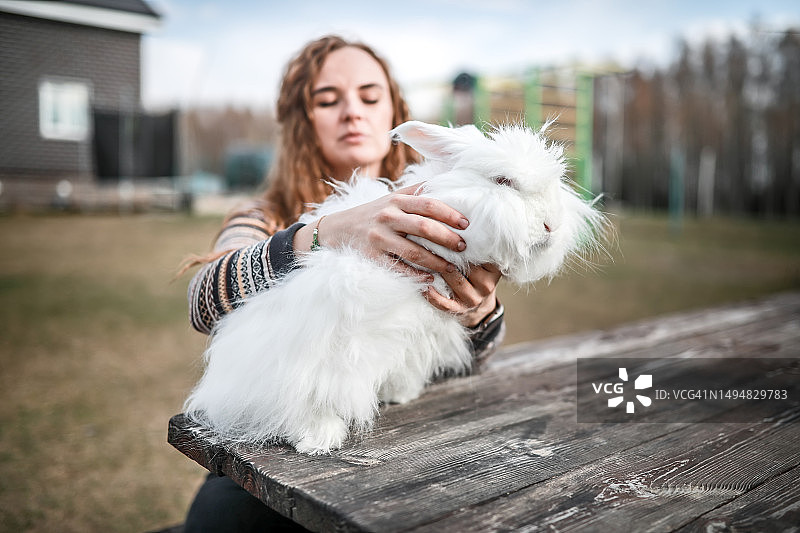 农场生活：中年妇女在舒适的兔子笼里照顾她的白色安哥拉兔，这是农场兔子养殖的一部分图片素材