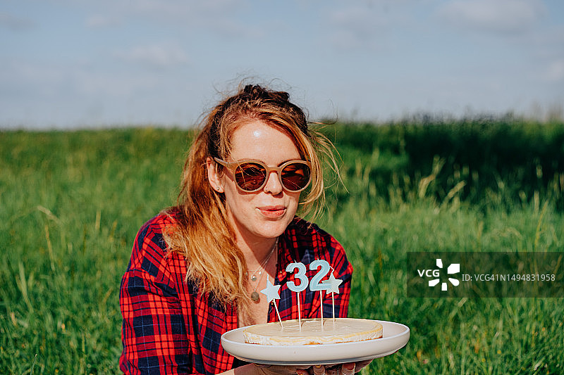快乐的红发女人在户外生日派对上拿着带蜡烛的生日蛋糕图片素材