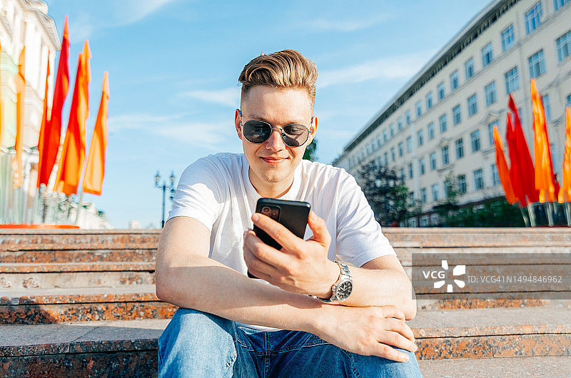 快乐的年轻人在城市公园的台阶上使用手机图片素材